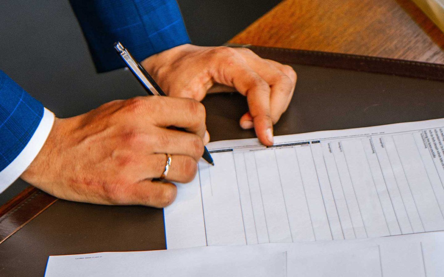 close up photo of a man's hand holding a pen and signing a document