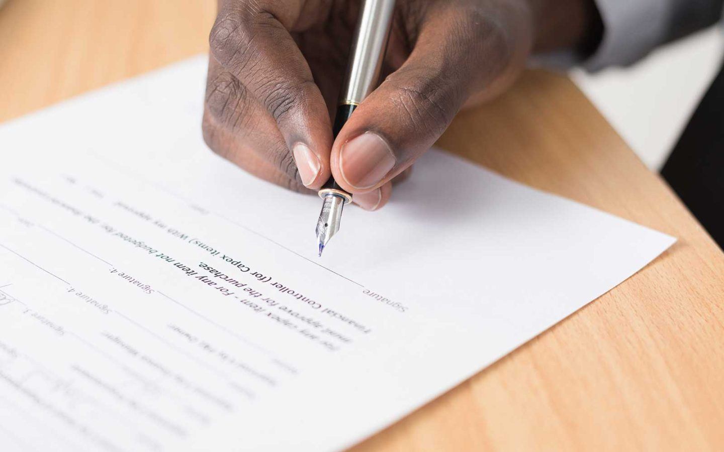 close up photo of a man's hand holding a pen and signing a document