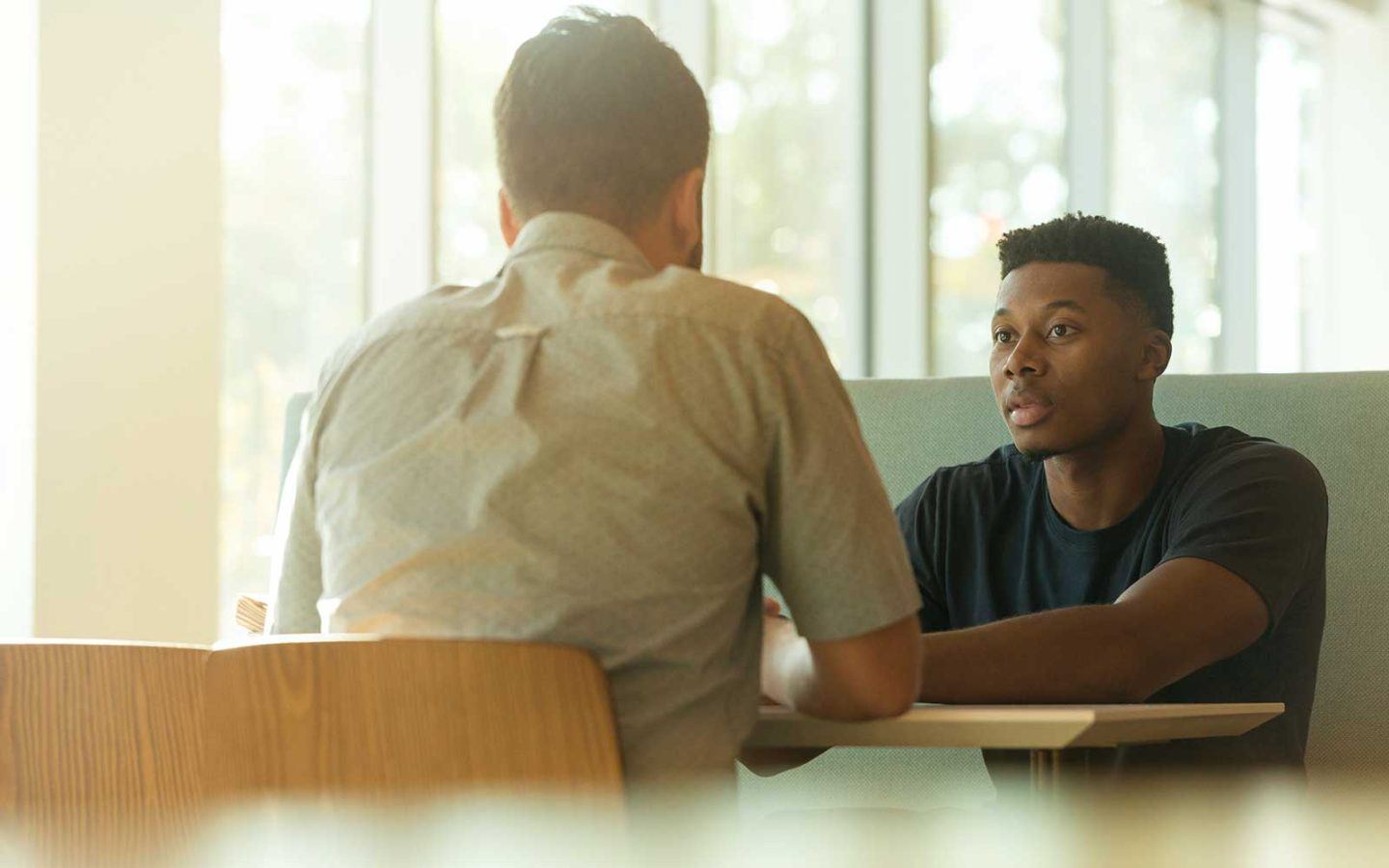 two men sitting at a table in an office having a discussion