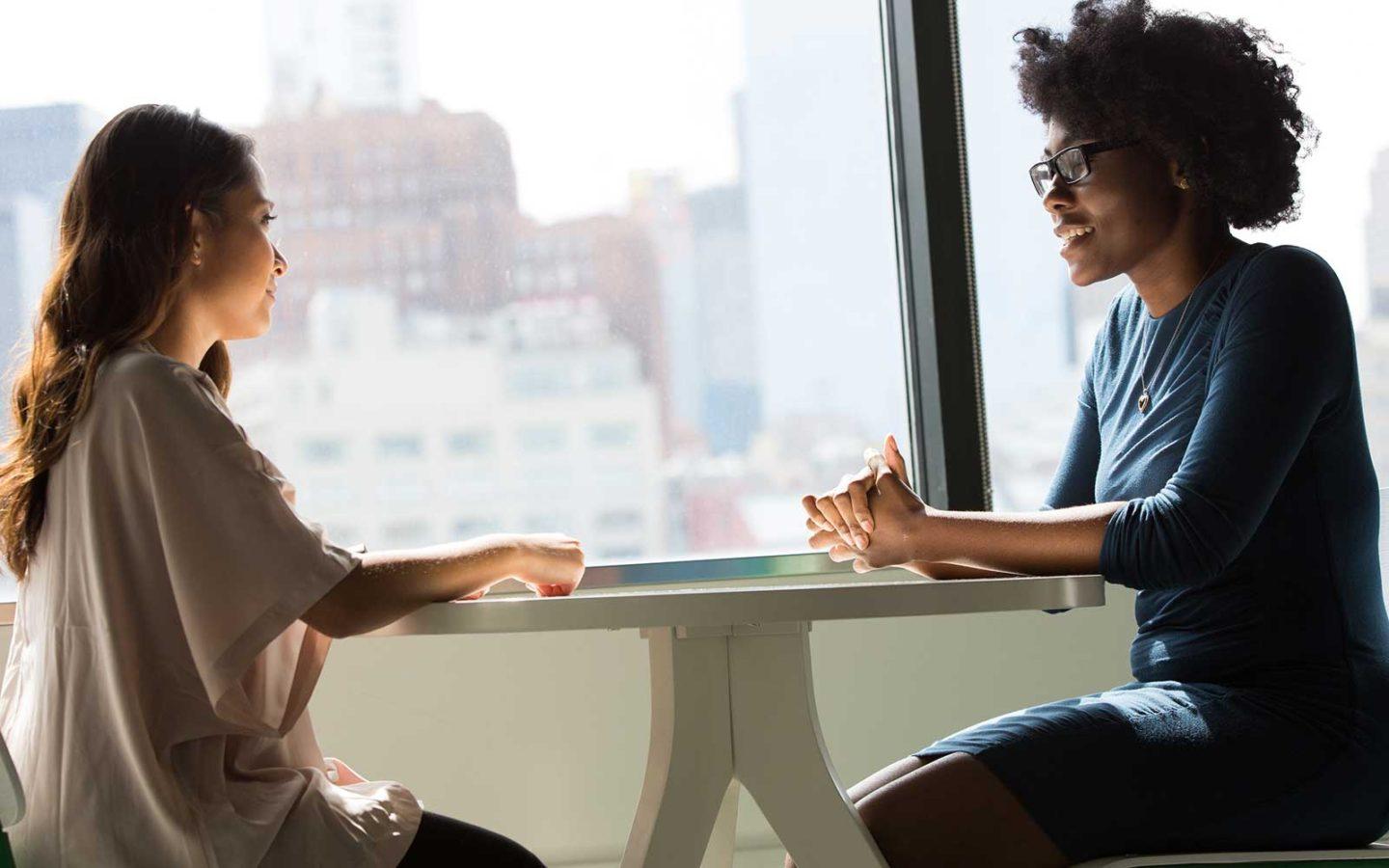 two women sitting at a white table in an office