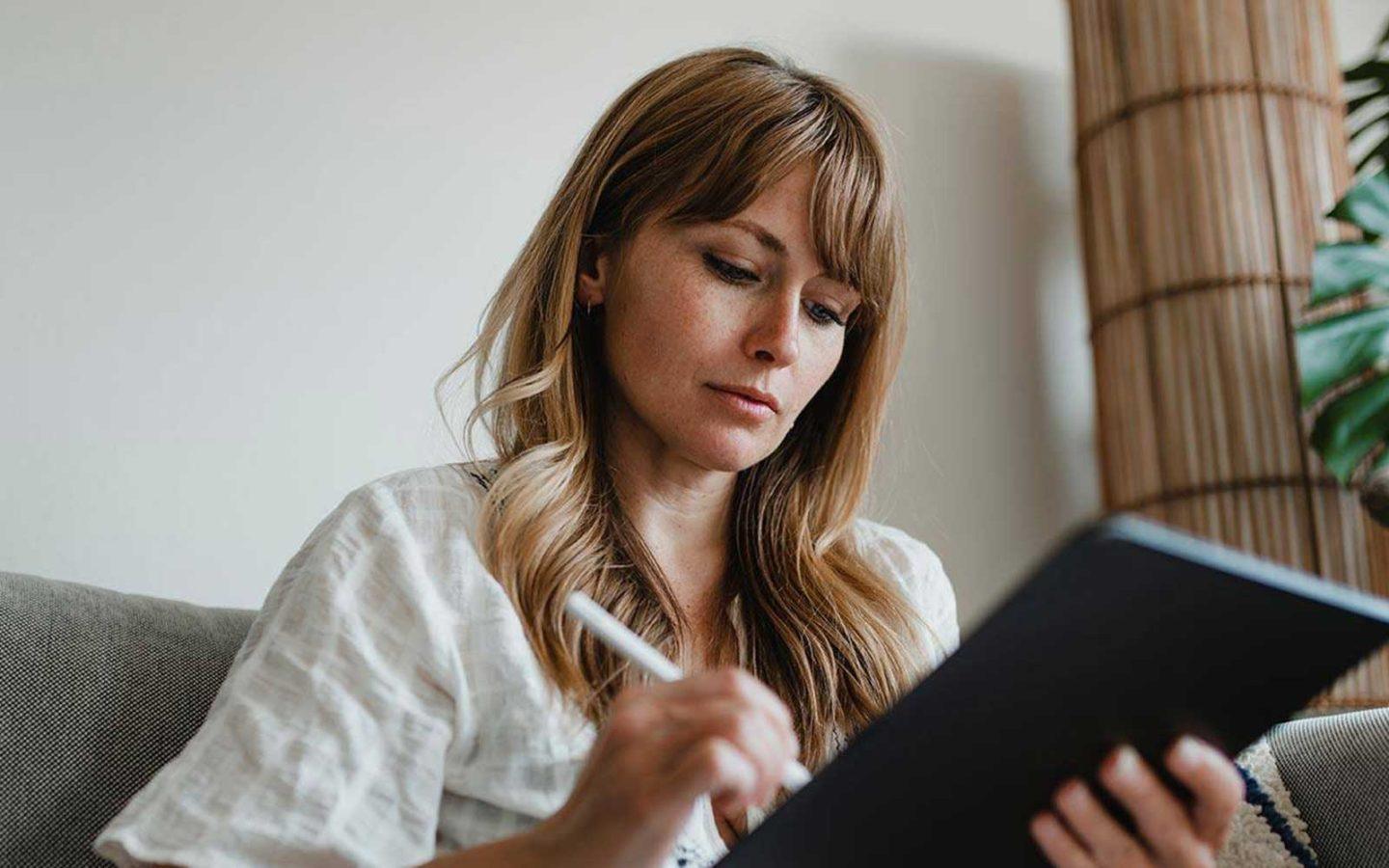 woman sitting on a grey couch working on a tablet