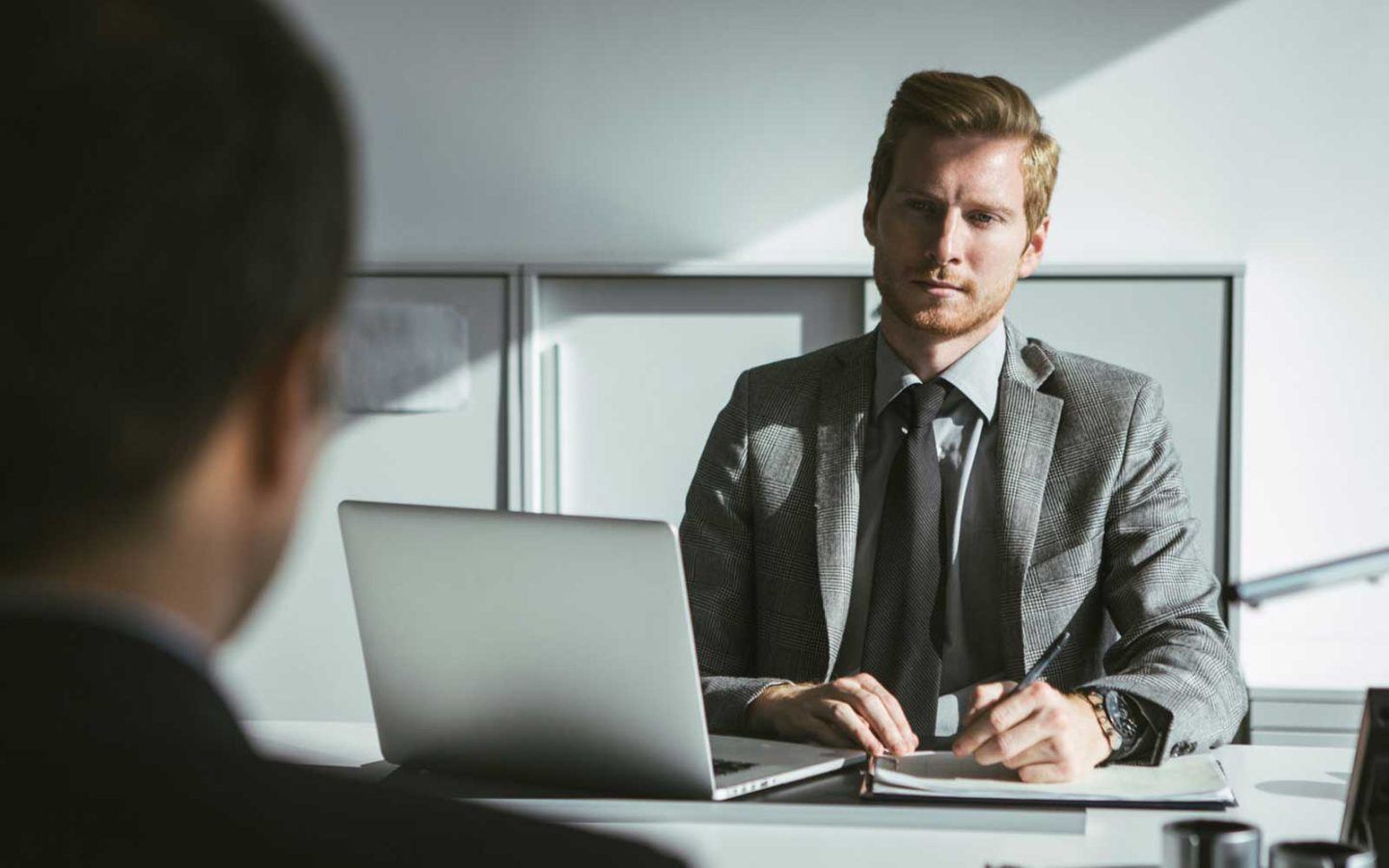 man in grey suite with a grey neck tie sitting in front of a computer